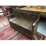 Antique oak box settle with a carved panel back above a hinged seat and carved panel front, 19th