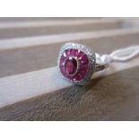 Platinum ring set central ruby bordered by a halo of calibre cut rubies and diamonds