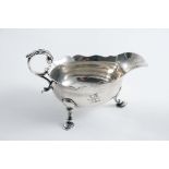 A GEORGE II CREAM BOAT on three legs, with a leaf-capped flying scroll handle and a wavy rim,