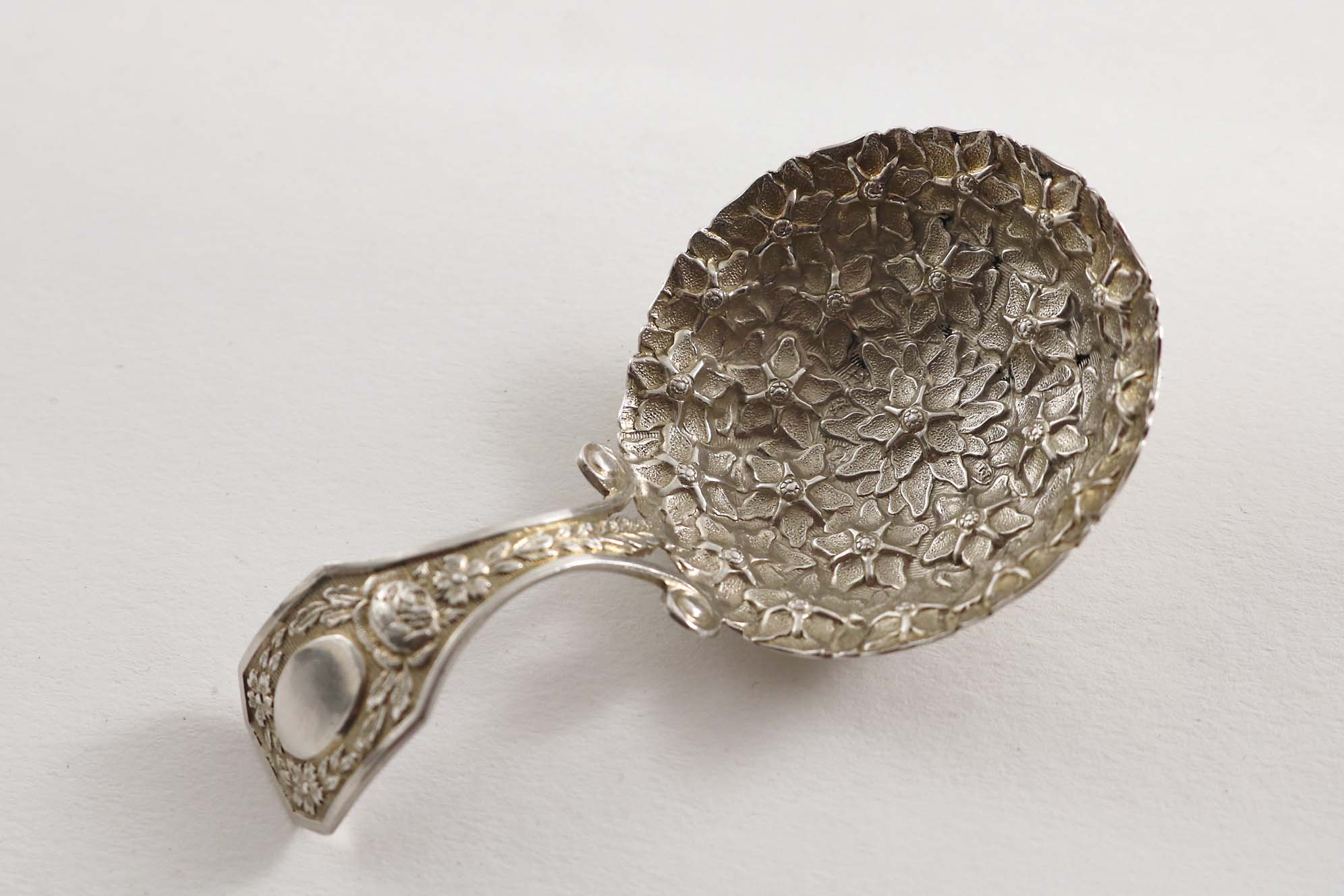 A GEORGE III CADDY SPOON the bifurcated stem with floral decoration and an oval cartouche, the