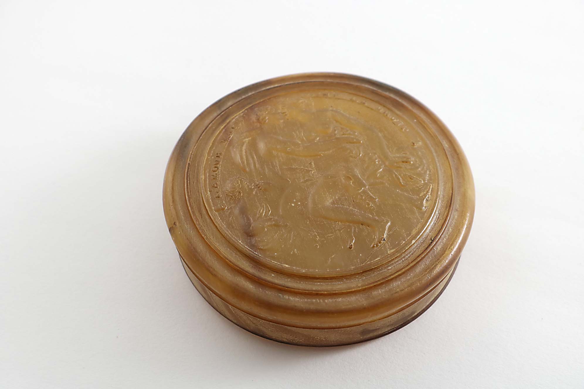 AN 18TH CENTURY CIRCULAR PRESSED HORN TOBACCO BOX with a moulded border, the cover depicting