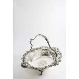 AN EARLY VICTORIAN SWING-HANDLED CAKE BASKET on four scroll feet, the shaped oval body pierced