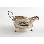 A GEORGE III SAUCE BOAT on three feet, with a punch-beaded rim and a leaf-capped, scroll handle by