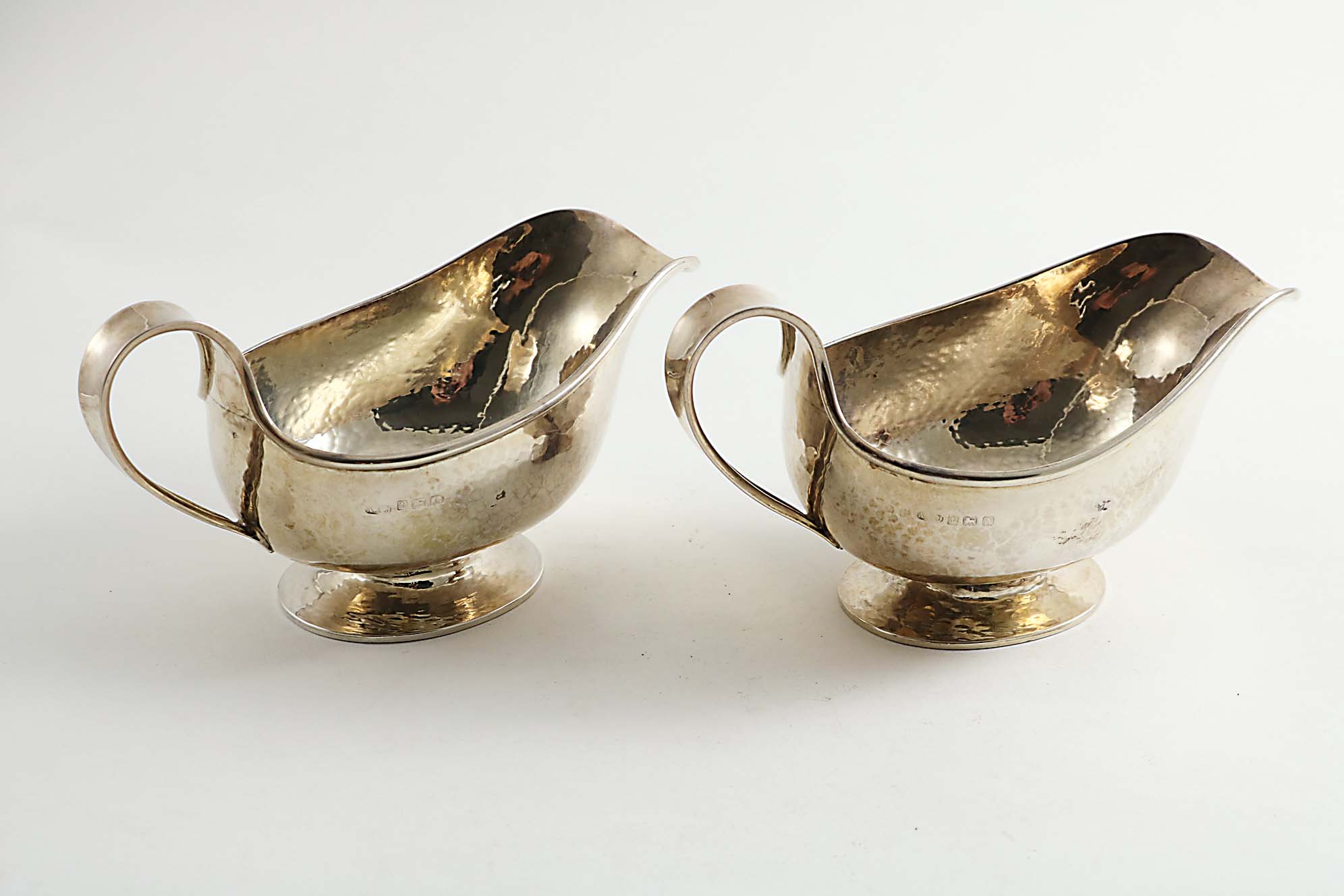 A PAIR OF EARLY 20TH CENTURY SAUCE BOATS with a hammered finish, loop handles and spreading oval