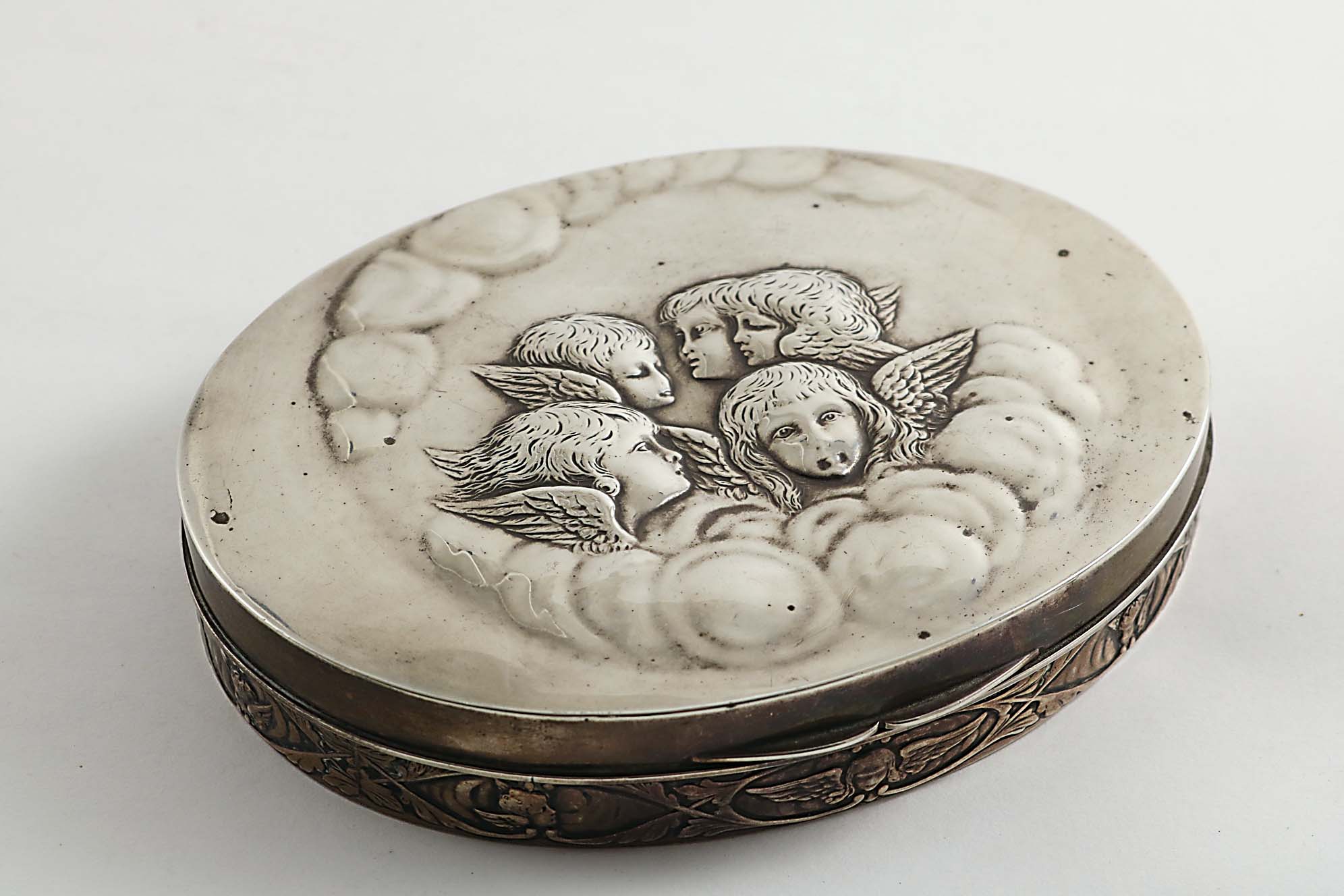 AN EDWARDIAN JEWELLERY OR DRESSING TABLE BOX of shallow oval form with a frieze of cherub masks