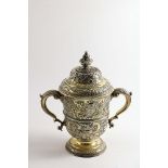 A GEORGE II SILVERGILT REPOUSSE-WORK CUP & COVER with twin, leaf-capped scroll handles, a campana