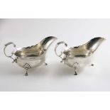 A PAIR OF GEORGE II SAUCE BOATS on three legs with wavy rims and leaf-capped, flying scroll handles,