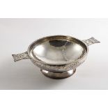 AN EDWARDIAN SHALLOW CIRCULAR DISH with a hammered finish, spreading foot and twin cast handles,