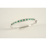 AN EMERALD AND DIAMOND HALF HINGED BANGLE the 18ct. white gold hinged bangle is set to one side with