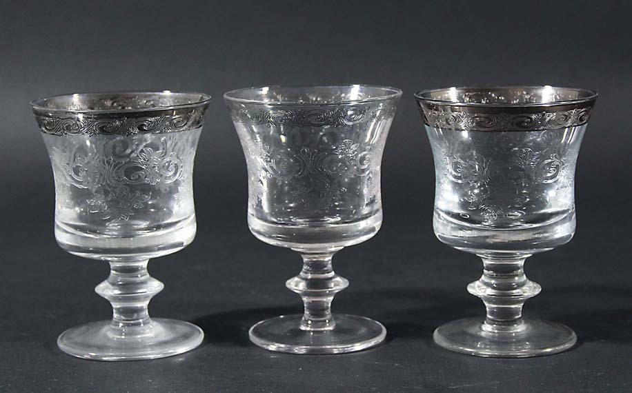 SET OF ELEVEN DRINKING GLASSES, the silvered rim above scrolling foliate decoration, knopped stem