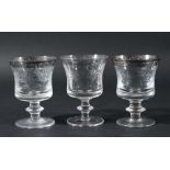 SET OF ELEVEN DRINKING GLASSES, the silvered rim above scrolling foliate decoration, knopped stem