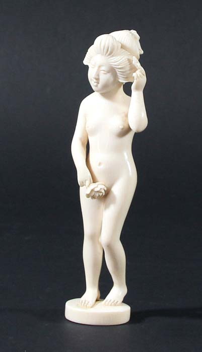 JAPANESE IVORY FIGURE OF A NUDE GEISHA, late 19th century, standing holding a flower and combing her