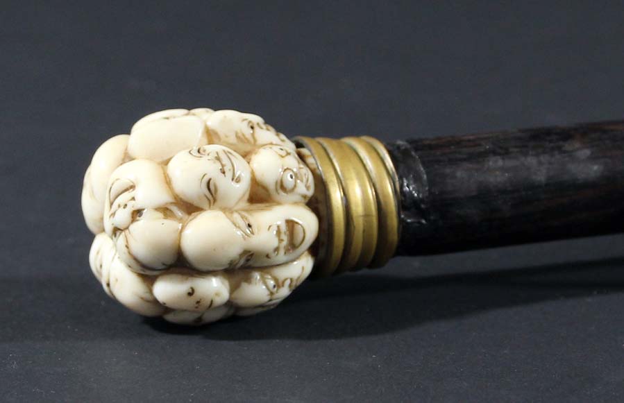 JAPANESE WALKING STICK, the ivory finial carved with numerous masks on an ebony shaft, length 85cm