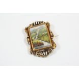 A SWISS ENAMEL AND GOLD BROOCH depicting a forest landscape with a lake and with mountains in the