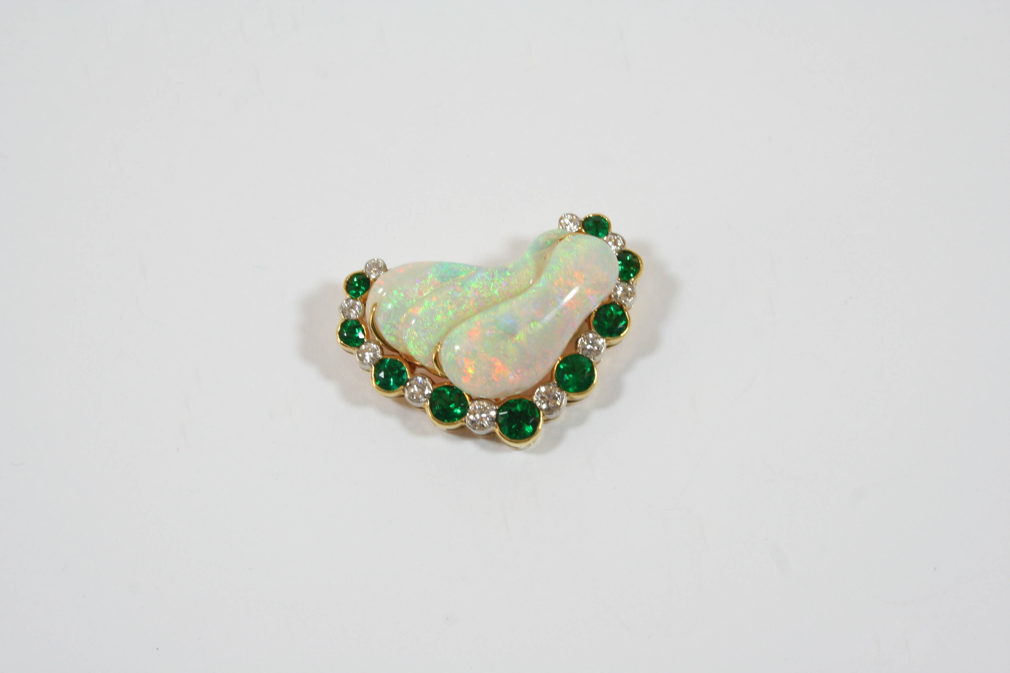 AN OPAL, EMERALD AND DIAMOND BROOCH formed with three overlapping sections of opal within a surround