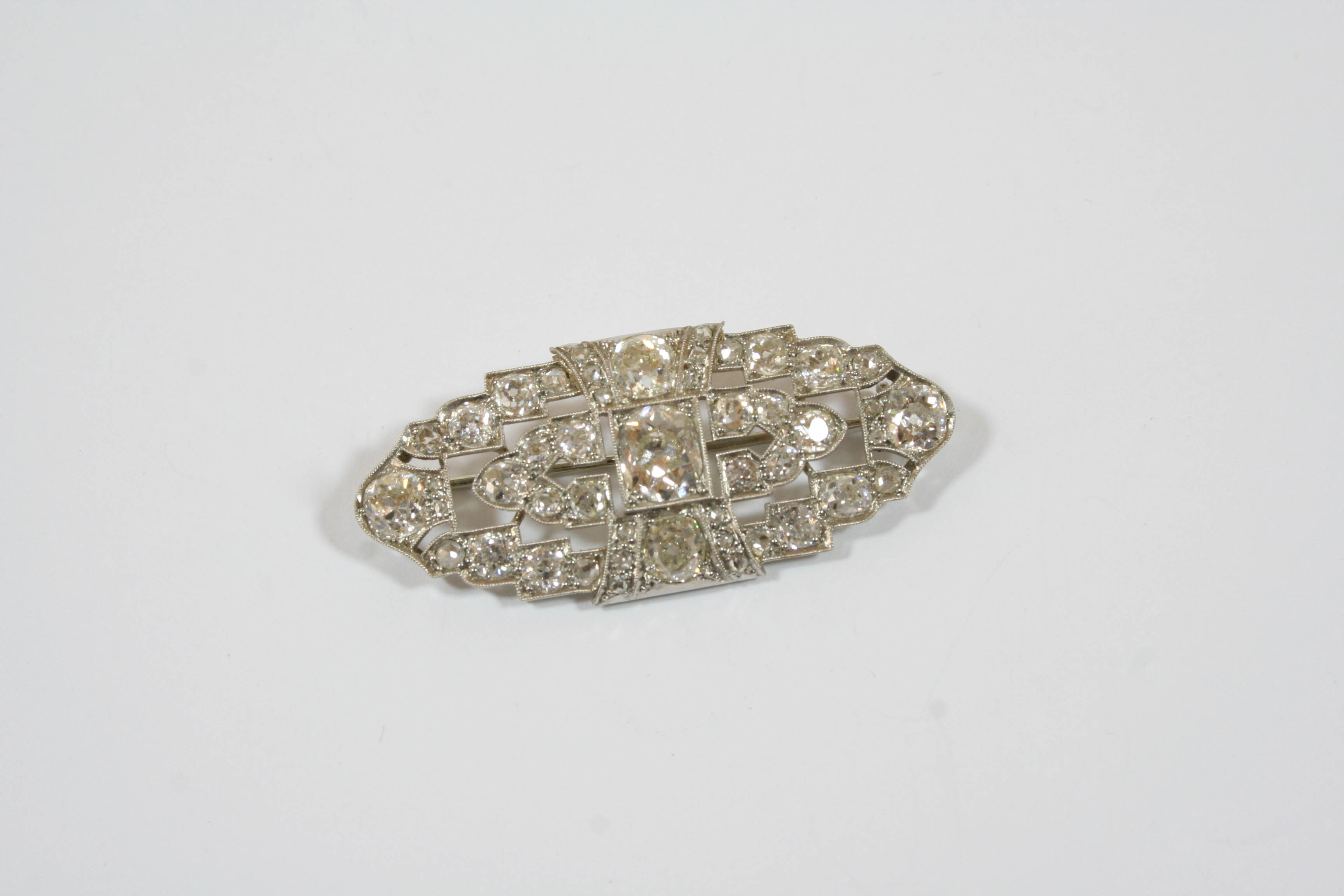 AN ART DECO DIAMOND BROOCH the openwork scrolling design is mounted with graduated cushion-shaped