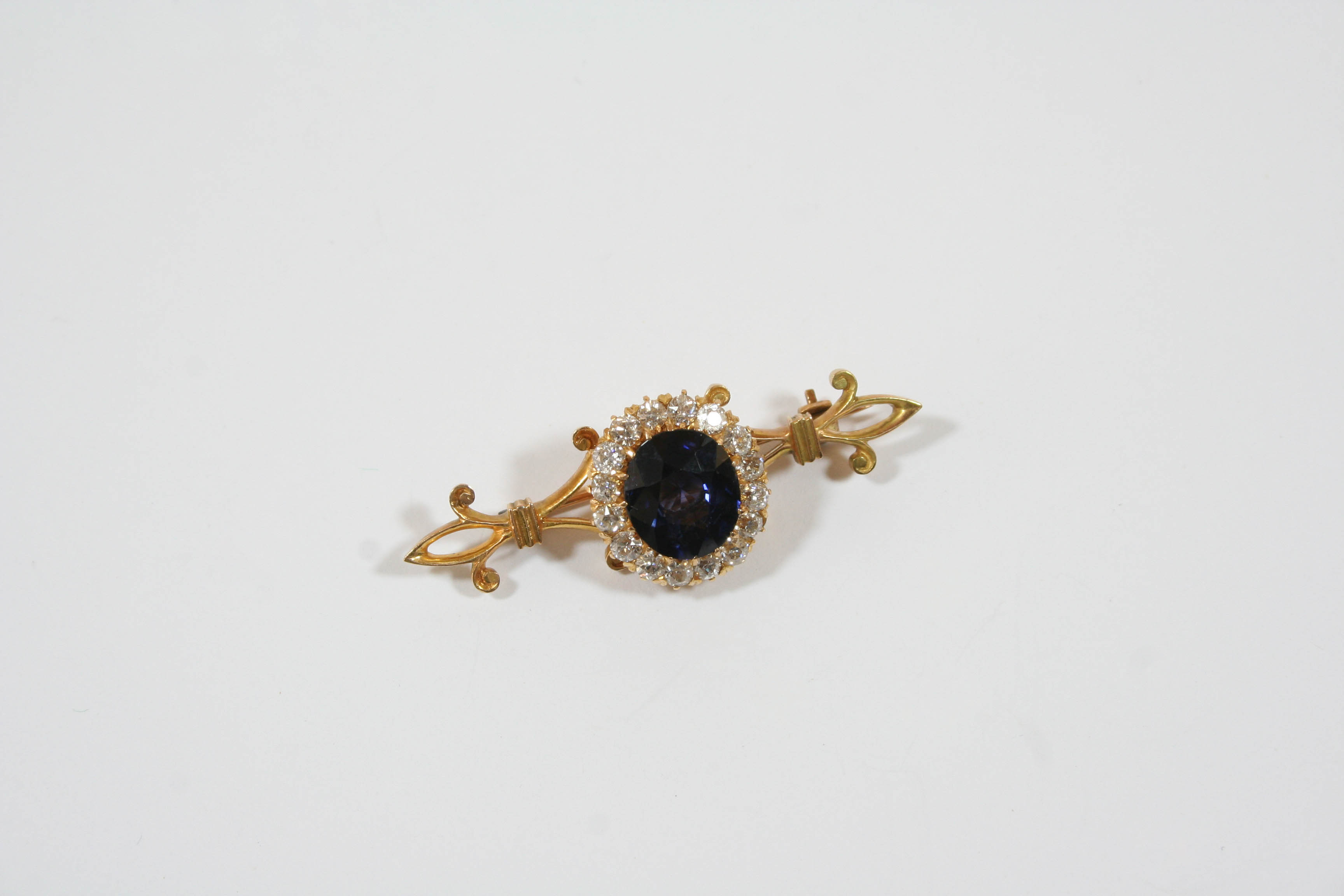 A SAPPHIRE AND DIAMOND CLUSTER BROOCH the oval-shaped sapphire is set within a surround of
