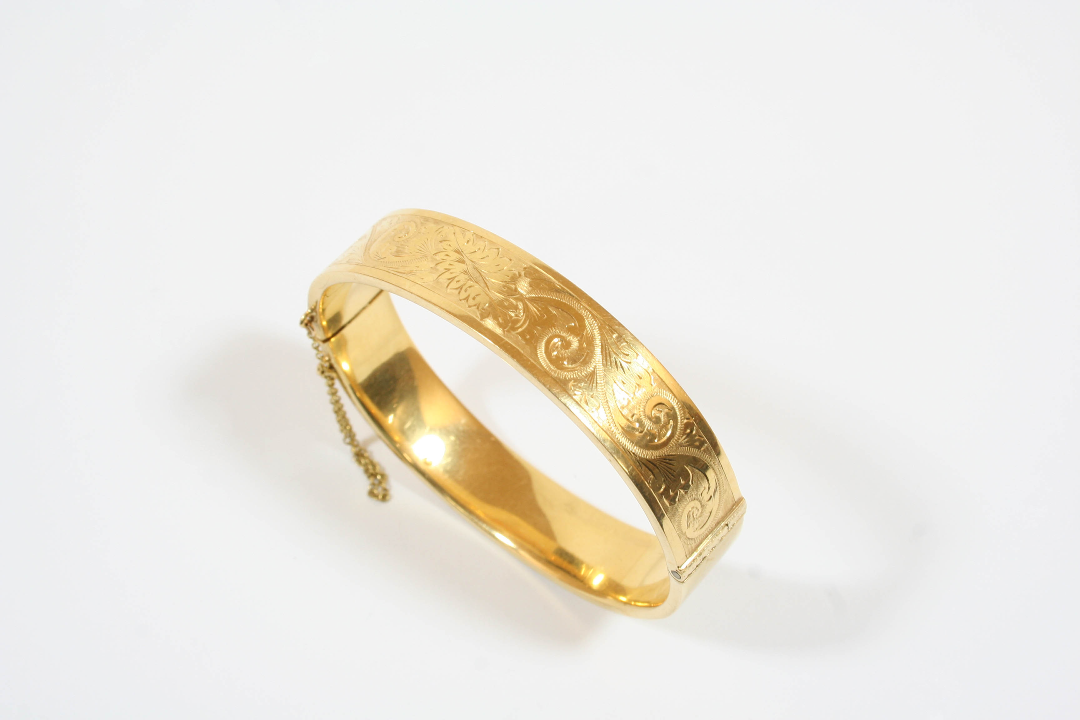 AN 18CT. GOLD HALF HINGED BANGLE with scrolling foliate decoration to one side, 27.6 grams.