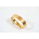 AN 18CT. GOLD HALF HINGED BANGLE with scrolling foliate decoration to one side, 27.6 grams.