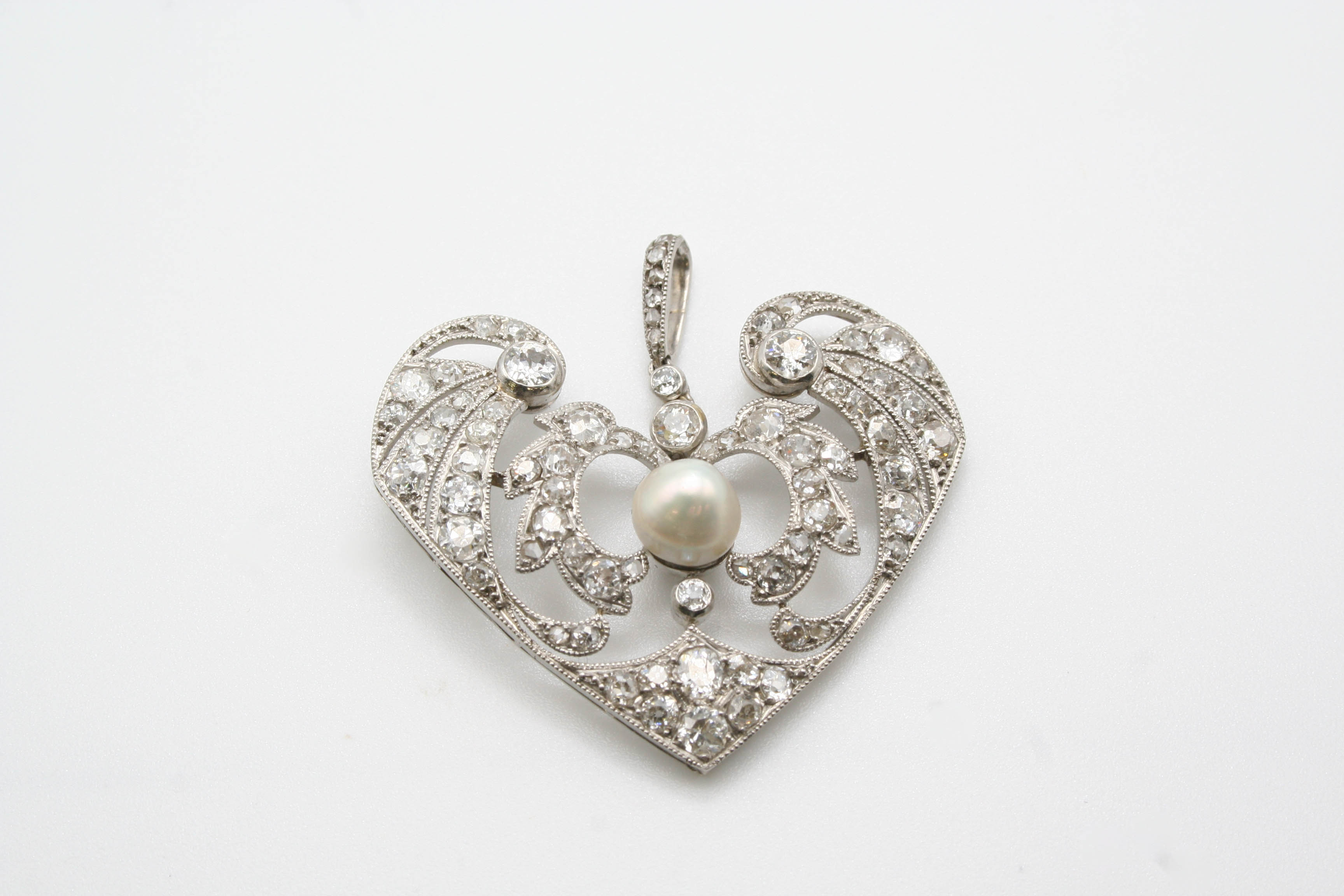 AN ART DECO DIAMOND AND PEARL PENDANT the openwork foliate scrolling mount is set with graduated old