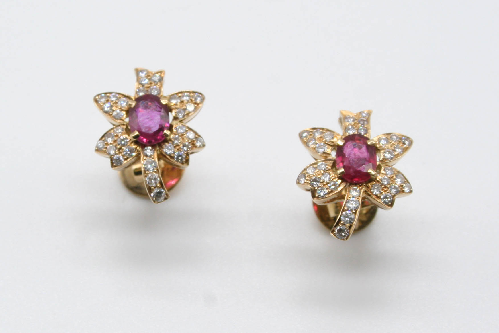 A PAIR OF RUBY AND DIAMOND FOLIATE STUD EARRINGS each earring is centred with an oval-shaped ruby,