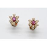 A PAIR OF RUBY AND DIAMOND FOLIATE STUD EARRINGS each earring is centred with an oval-shaped ruby,