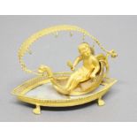 GILT METAL RING STAND, modelled as a cherub seated in a gondola beneath a ribbon shade on a