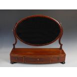 A 19th century mahogany and boxwood lined dressing table mirror, the oval mirror plate on a bow