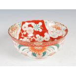 A Japanese red ground porcelain bowl, late 19th/ early 20th century, decorated with panels of long