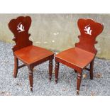 A pair of mahogany hall chairs, the shaped back with painted Armorials, the solid plank seats raised