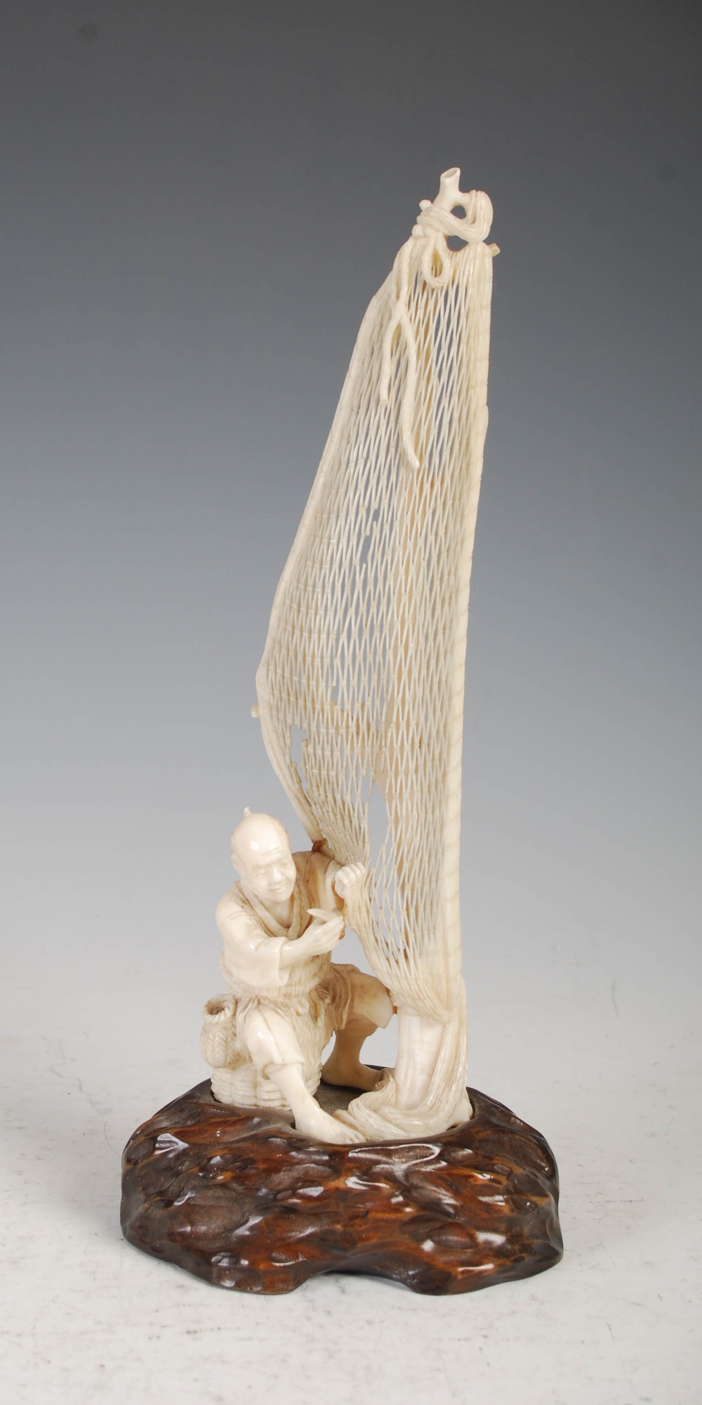 A Japanese ivory okimono of a fisherman tending net, Meiji Period, on carved wood stand, overall