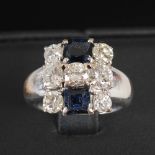A white metal sapphire and diamond set cocktail ring, set with a row of three brilliant cut diamonds