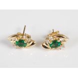 A pair of yellow metal, emerald and diamond cross-over style earrings, each set with an oval faceted