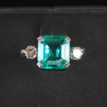 An Art Deco style white metal, emerald and diamond three stone ring, centred with an emerald cut