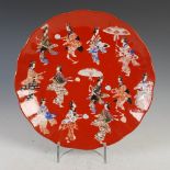 A Japanese red ground porcelain dish, late 19th/early 20th century, decorated with twelve bijin,