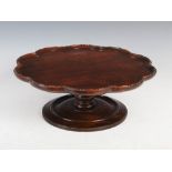 A George III style mahogany lazy susan, the shaped circular top raised on a baluster column and