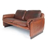 A 1970's brown leather two seater sofa on faux rosewood slab feet,