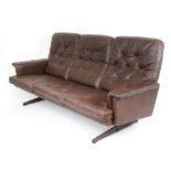 A 1970's brown button upholstered three seater sofa on black and faux rosewood supports