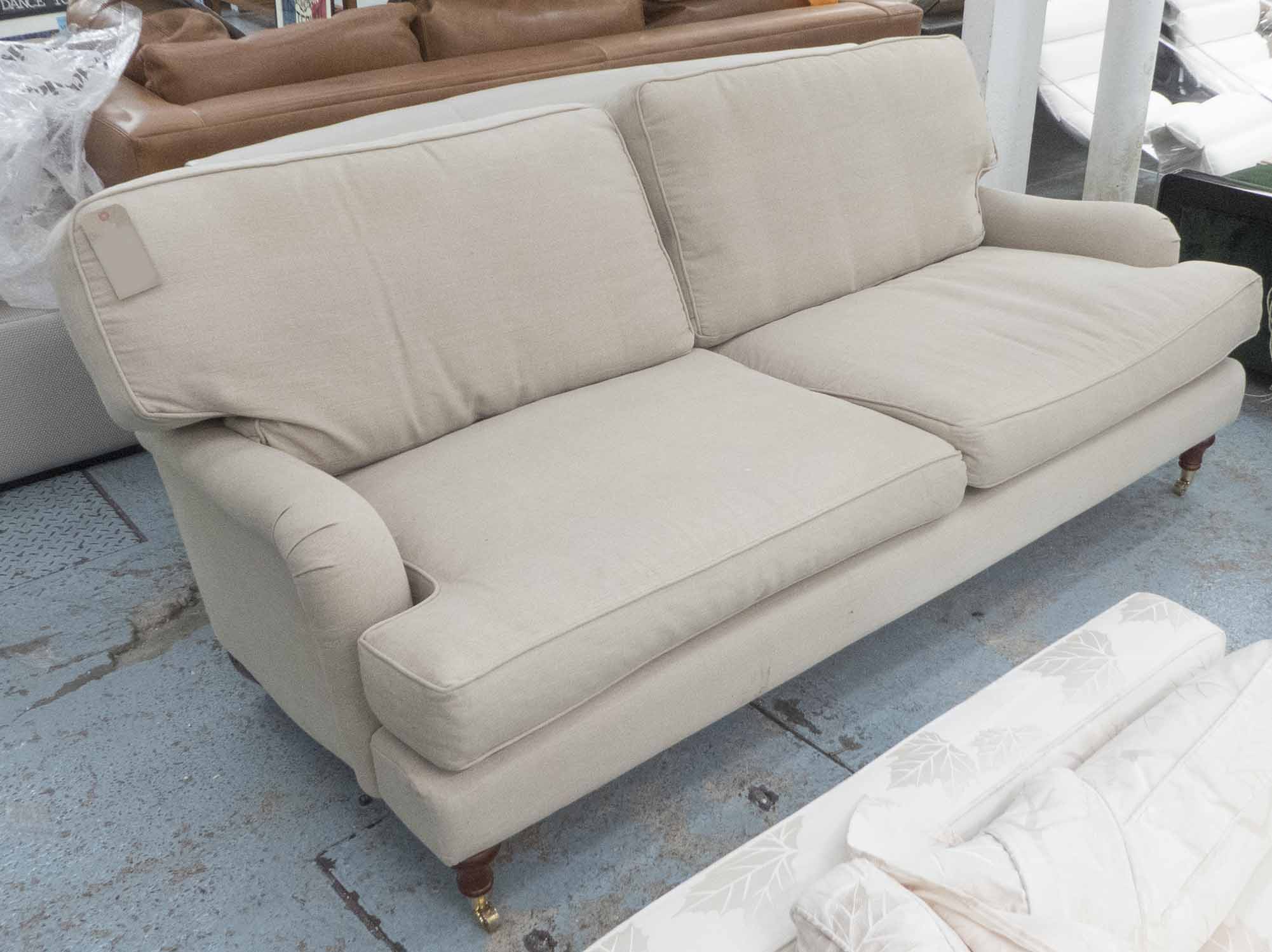 SOFA, two seater, Howard style, in beige fabric on turned castor supports, 212cm L.