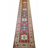 FINE KAZAK RUNNER, 464cm x 85cm, of multiple medallions on ruby field within ivory borders.