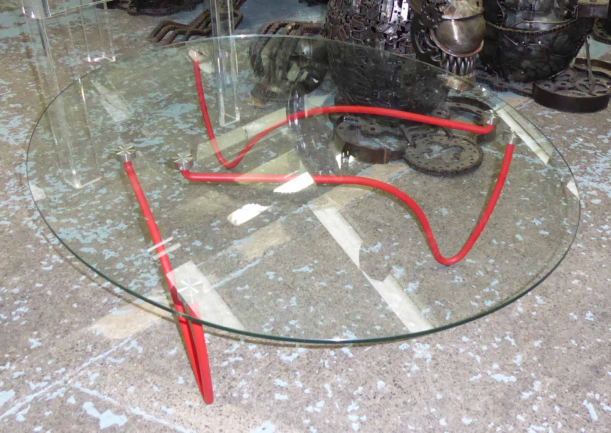 OCCASIONAL TABLE, oval glass top on red metal supports, 109cm W x 89cm D x 31cm H.