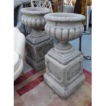 GARDEN URNS ON STANDS, a pair, weathered composite stone, 100cm H.