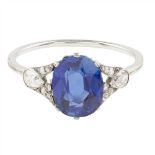 A sapphire and diamond set ring claw set with an oval cut sapphire, each shoulder millegrain set