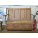 A pine bench with panelled back and hinged seat on a later panelled front 127cm wide