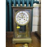 A late 19th century brass mantel clock, with glazed sides, and enamel dial on columns, the dial with