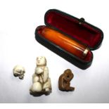 Two ivory netsuke in the form of a skull and a figure, another monkey netsuke and an amber cheroot