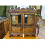 An Edwardian oak smokers cabinet, the scroll carved top over glazed doors enclosing a fitted