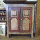 An Alpine style painted pine cupboard, the moulded cornice over a pair of panelled cupboard doors on