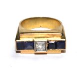 A gold colour metal ring, set with central diamond and two square sapphires either side
