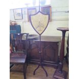 An early Victorian pole screen, the shield shape screen on a baluster turned stem and tripod base,